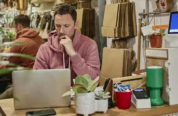 Dono de pequena empresa olhando para o laptop com uma expressão pensativa e preocupada, analisando por que seu concorrente aparece no topo do Google.