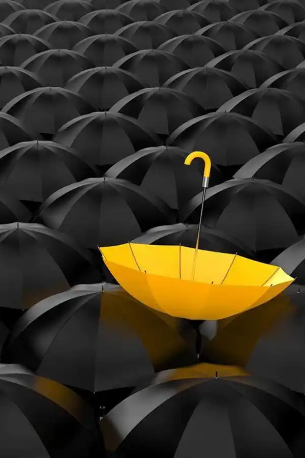 Guarda-chuva amarelo se destacando em meio a uma multidão de guarda-chuvas pretos, simbolizando o diferencial e a estratégia para uma marca ser única.